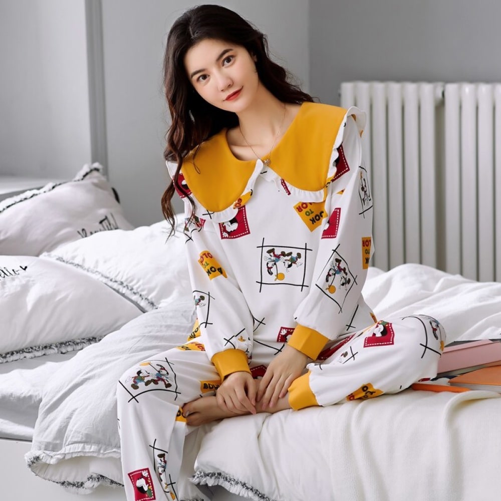 Pigiama di alta qualità da donna con maniche lunghe e polsini in cotone, indossato da una donna seduta su un letto in una casa