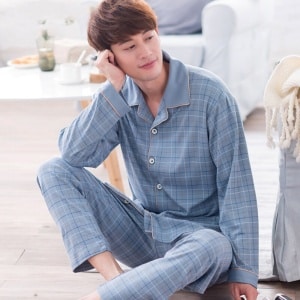 Pigiama trendy in cotone blu chiaro a quadri per uomo, indossato da un uomo seduto su un tappeto in una casa