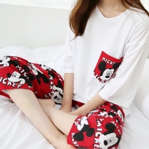 Pigiama a due pezzi rosso e bianco con motivo Mickey indossato da una donna seduta su un letto alla moda