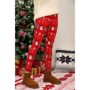 Leggings rossi con stampa natalizia per donne, indossati da una donna davanti a un albero di Natale in una casa