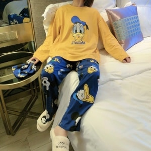 Pigiama da donna Disney Donald, giallo senape e blu, indossato da una donna seduta su un letto in una casa