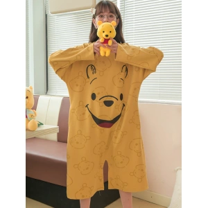 Pigiama largo da donna Winnie the Pooh giallo senape indossato da una donna davanti a un divano in una casa