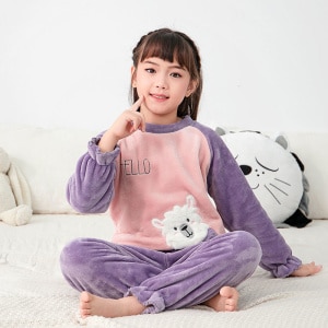 Set di pigiama in pile per bambini di colore viola, indossato da una bambina seduta su un letto in una casa