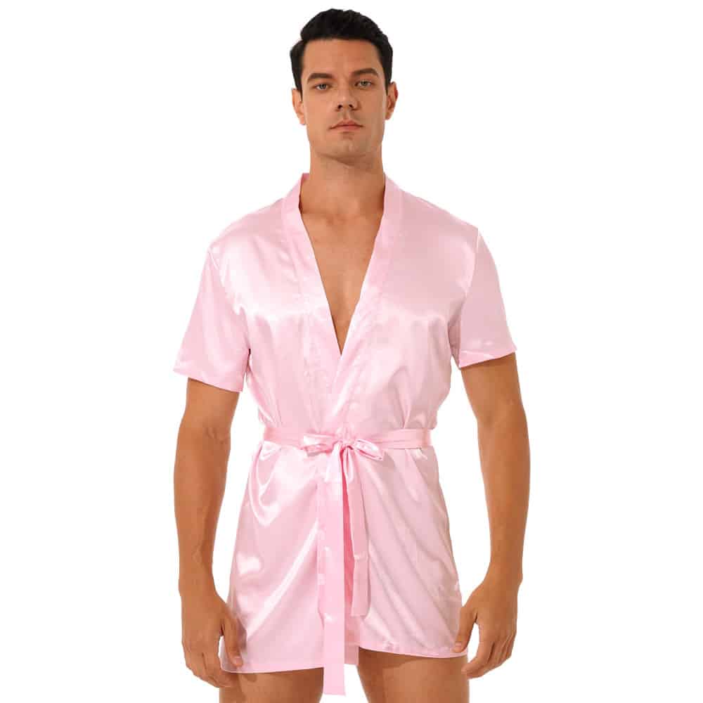 uomo dai capelli scuri in piedi con un pigiama kimono di raso rosa legato in vita con una cintura