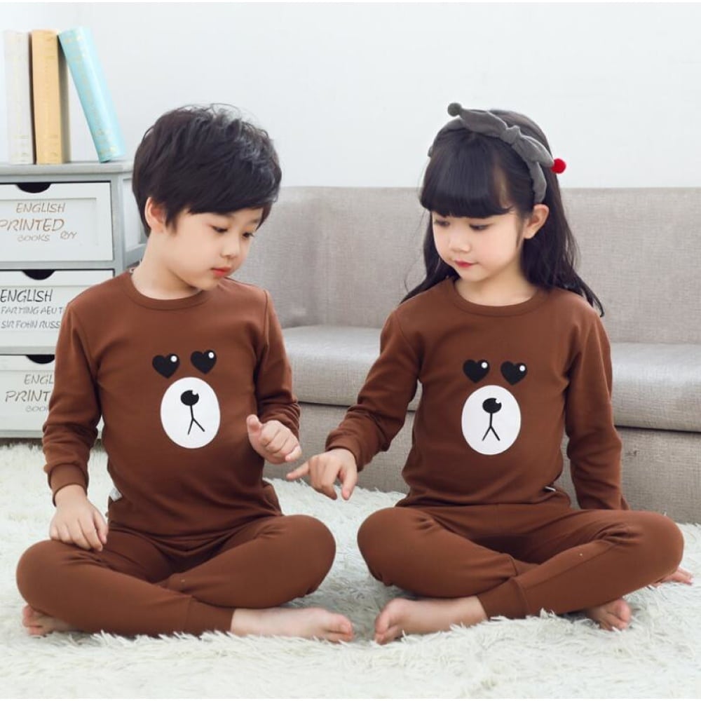 Pigiama primaverile marrone con motivo di orso per bambini con due bambini che indossano il pigiama e un divano di sfondo
