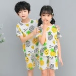 Pigiama bianco a due pezzi con ananas, due bambini che indossano il pigiama e uno sfondo grigio