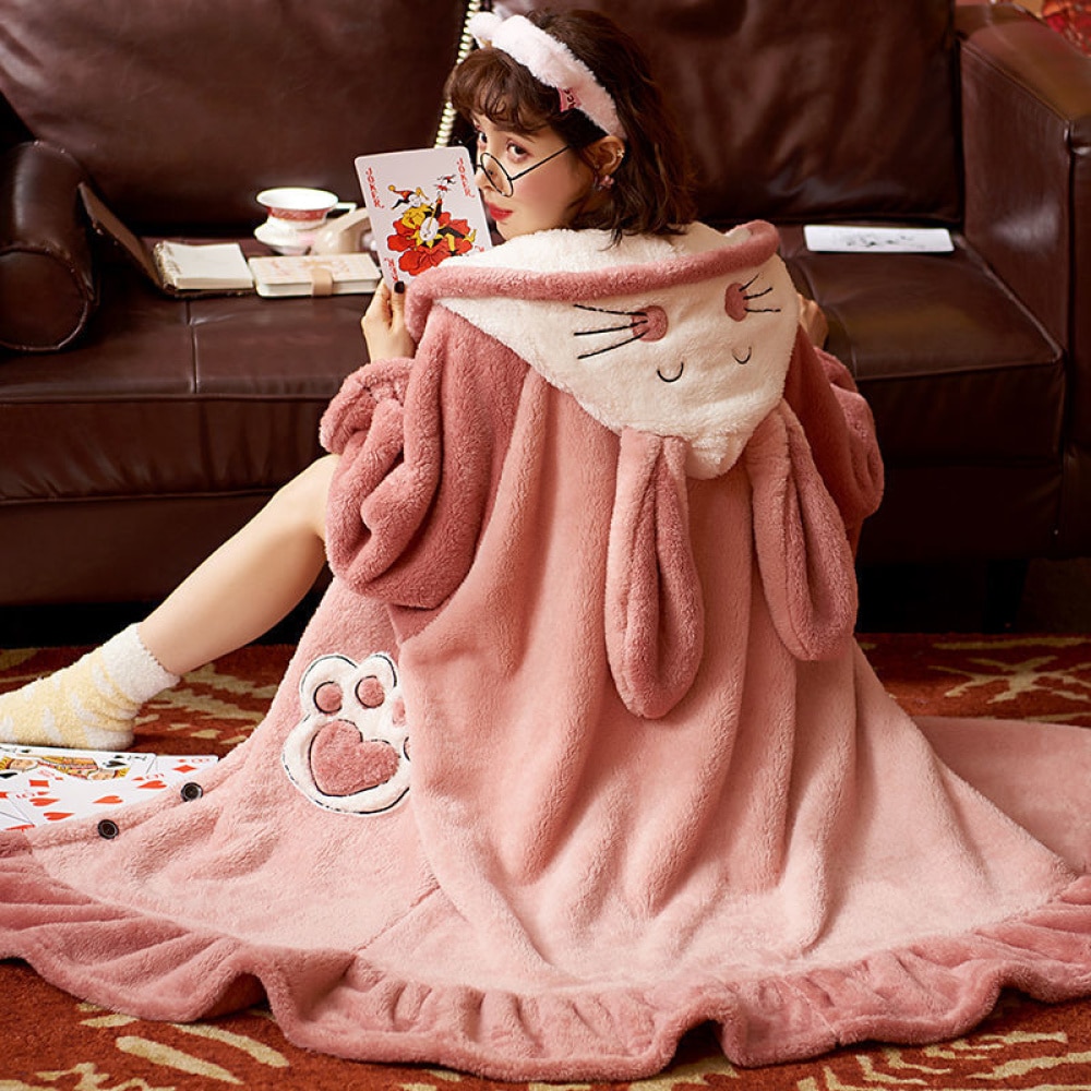 Pigiama lungo da donna con cappuccio in pile con pelliccia di coniglietto rosa e sfondo di divano
