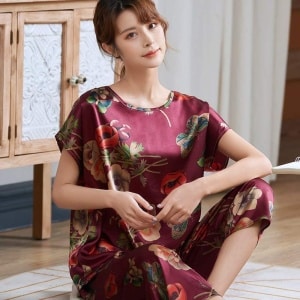 Pigiama estivo in raso di seta rosso con stampa floreale per donna, indossato da una donna seduta su un tappeto in una casa