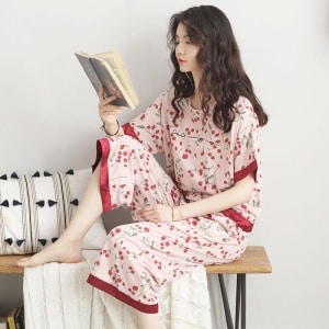 Pigiama da donna con maniche a pipistrello e stampa di fiori rossi indossato da una donna che legge un libro seduta su una sedia in una casa