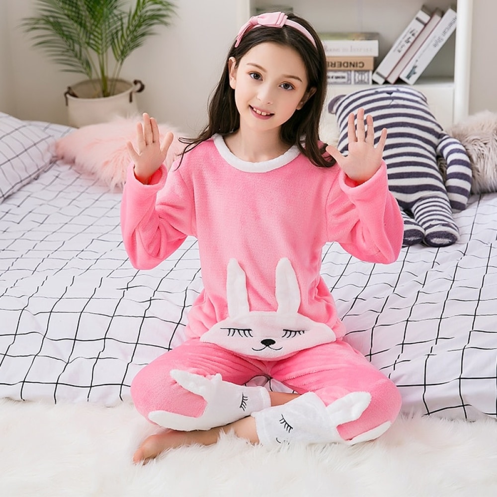 Pigiama di flanella rosa con stampa di coniglietti per una ragazza che indossa una fascia per capelli seduta su un letto in una casa