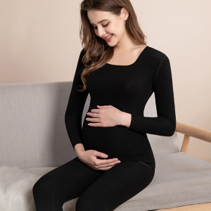 giovane donna incinta seduta in pigiama nero, sorridente mentre si tocca la pancia rotonda