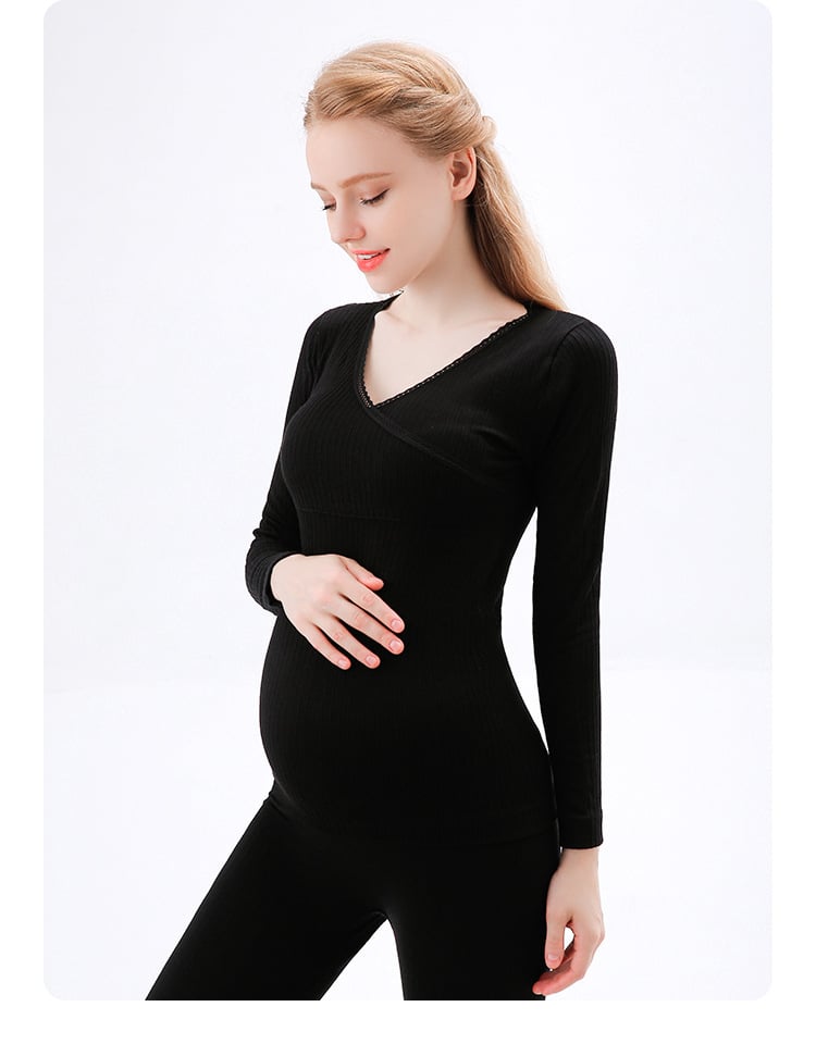 donna incinta che si tocca la pancia con una mano, con indosso un pigiama nero composto da pantaloni e maglia a maniche lunghe