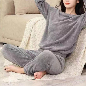 giovane donna che indossa un pigiama grigio di pilou pilou, è seduta su un plaid accanto a un divano, sul pavimento, con le mani incrociate dietro la testa